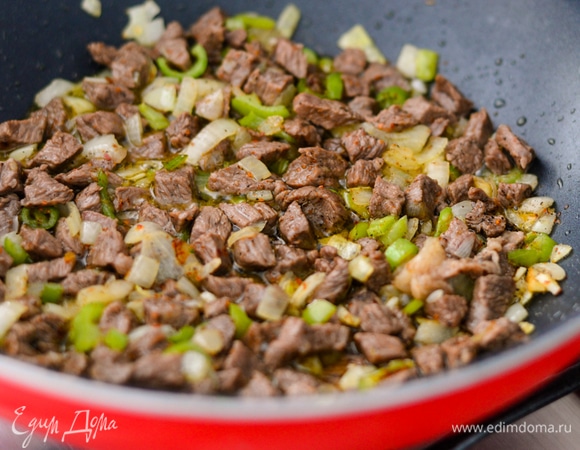 Пока баклажаны отдыхают в воде, нарежьте лук (не очень мелко) и перец (я смешиваю острый и сладкий перцы), обжарьте их в оливковом масле до полуготовности, затем добавьте специи, соль и мясо, продолжайте обжаривать на медленном огне 5–10 минут.