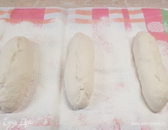 Полотенце посыпать мукой. Тесто разделить на три части. Из каждой заготовки сформировать батон. Положить швом вверх, накрыть пленкой и оставить на 1 час.