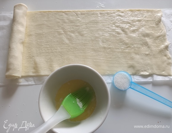 Растопить сливочное масло и смазать одну половину теста. Посыпать сахаром. Свернуть тесто в рулет, при каждом загибе надавливая пальцами.