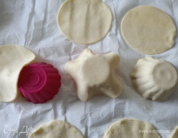 Форму для маффинов перевернуть верх дном. Сверху выложить слоеное тесто, слегка придавить пальцами.
