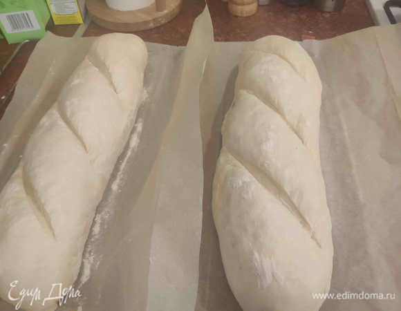 А тем временем разогреваю духовку до 220–240°C. Причем ставлю туда же противень, на котором буду печь потом, и пустую емкость для пара (я использую небольшую тефлоновую форму для выпечки). Пусть разогреваются тоже. Смазываем тихонько батончики водой. Совсем немного. И делаем острым ножом диагональные надрезы. Основательные, не стесняйтесь. <br />
Духовка разогрелась. Выдвигаем противень, аккуратно перекладываем на него батончики вместе с бумагой для выпечки. Возвращаем противень в духовку, а в разогретую емкость для пара наливаем стакан кипятка. И быстро закрываем духовку. С паром выпекаем 7–8 минут. После чего емкость с водой убираем, духовку проветриваем. Допекаем батончики еще в течение 7–8 минут.