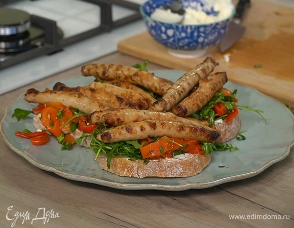 Обжаренный хлеб смазать сливочным сыром, сверху выложить заправленные овощи и колбаски. 