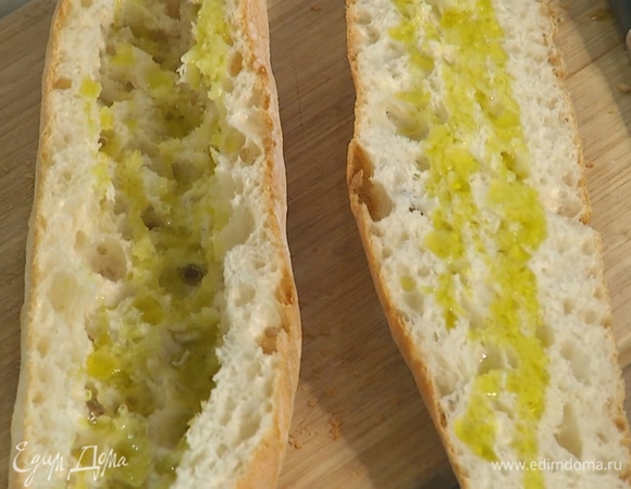 Багет разрезать вдоль пополам, из нижней части вынуть мякиш, затем обе половинки сбрызнуть внутри оливковым маслом.