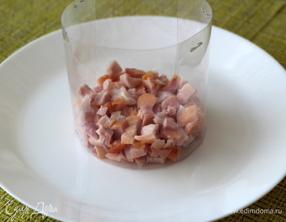 Начинаем формировать салат. На тарелку ставим кольцо/форму для салата, я всегда пользуюсь ацетатной пленкой, сворачиваю нужный диаметр и скрепляю степлером. Выкладываем первым слоем копченые кусочки.