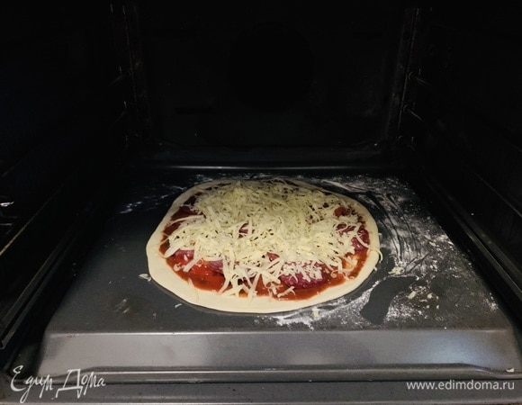 Припыляем мукой противень с обратной стороны — так пицца легко съезжает после выпекания. Можете использовать любую другую форму, непринципиально. Перекладываем на него тесто и заправляем пиццу.