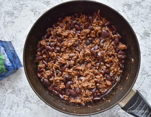 Фасоль замочить на ночь в воде. Промыть, залить чистой водой и отварить до готовности. В сковороде разогреть оливковое масло, выложить мелко нарезанный лук и чеснок. Всыпать тмин, паприку, кориандр, хлопья перца чили. Добавить говяжий фарш и обжарить. К обжаренному фаршу добавить томатную пасту, помидор, нарезанный кубиком, и отваренную фасоль, посолить. Влить немного отвара из-под фасоли (0,5 стакана) и потушить под закрытой крышкой до выпаривания лишней влаги.