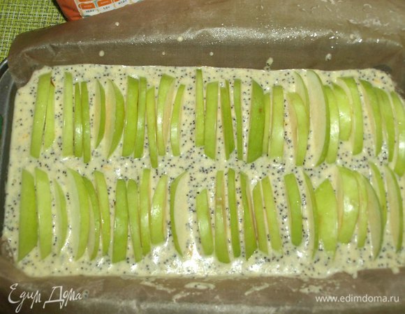 Форму для запекания выстелить бумагой для выпечки, чтобы оставались свободные края. У меня форма для кекса 22х13. Смазать растительным или сливочным маслом. Посыпать сахаром. Тесто еще раз перемешиваем и выкладываем в форму. Сверху как можно плотнее выкладываем дольки яблок.