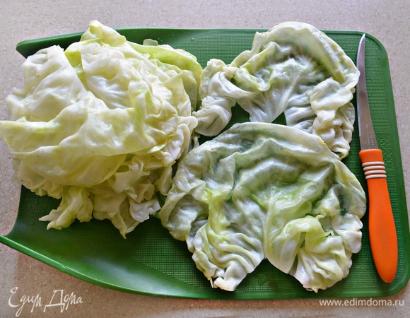 Разобранные листья капусты выложите на разделочную доску. Вырежьте толстые части у основания капустного листа.
