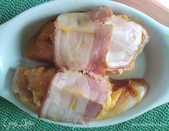 Каждый кусок завернуть в бекон. Форму смазать растительным маслом и выложить филе. Сверху сбрызнуть немного маслом. Духовку разогреть до 210°C. Запекать 30 минут. Через 20 минут полить курицу выделившимся соком.