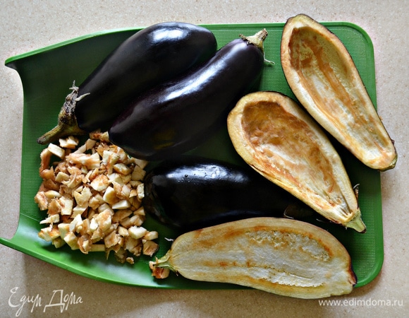 Промойте баклажаны, разрежьте их пополам и аккуратно, не повредив стенки, с помощью ложки выньте мякоть. Слегка посолите баклажаны внутри, сбрызните оливковым маслом, положите на противень срезом вниз, накройте фольгой и запекайте 7–10 мин. Затем переверните баклажаны срезом вверх, прикройте фольгой и запекайте еще 7 минут до размягчения баклажанов.
