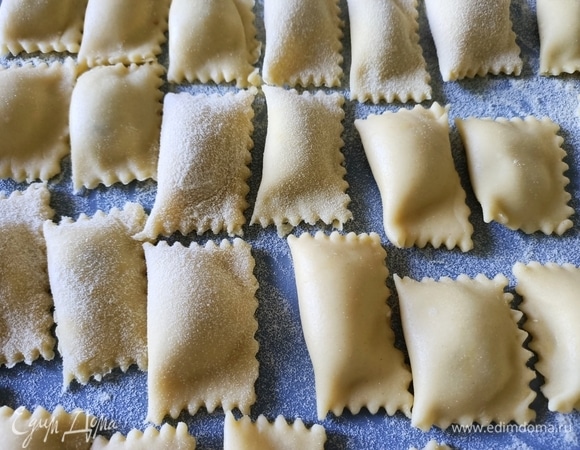 Стол посыпать манной крупой. Раскатать тесто. Выложить начинку на расстоянии 3 см друг от друга. Накрыть начинку тестом. Разрезать равиоли дисковым ножом с зубчатыми краями. Опустить равиоли в кипящую воду и варить до готовности около пяти минут.