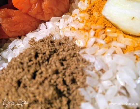 В чашу мультиварки выложите рис, добавьте специи, курагу, чеснок и масло. Залейте кипяток и включите программу «рис».