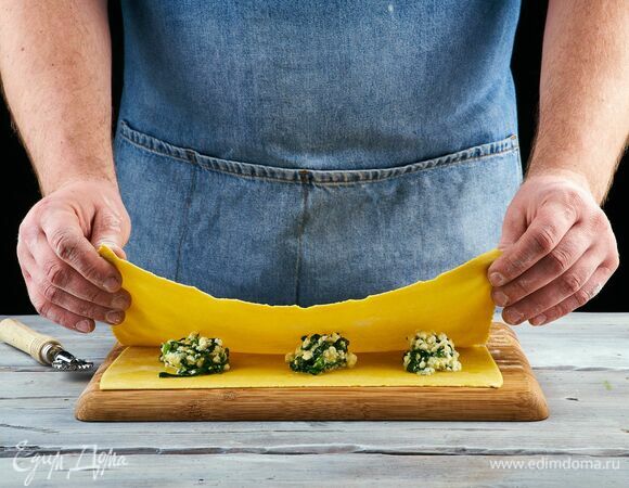 Отдохнувшее тесто выложите на рабочую поверхность, присыпанную мукой, и раскатайте его в очень тонкий пласт. <br />
На одну половину теста поместите начинку, выкладывая по одной чайной ложке на некотором расстоянии друг от друга. Накройте второй половиной теста.