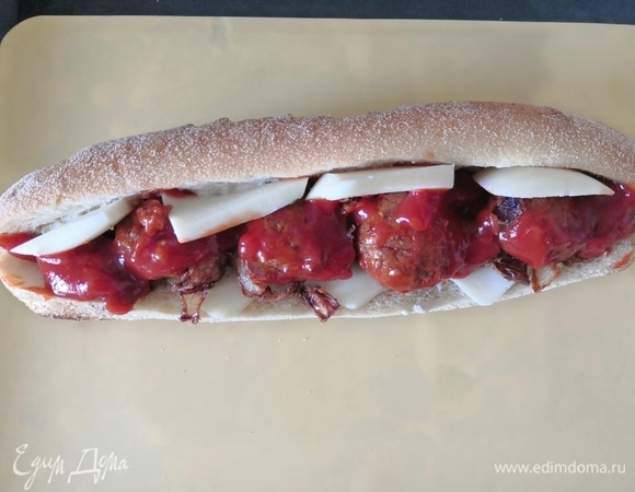 Разогрейте духовку до 200°C. Разрежьте багет пополам, оставив его соединенным с одной стороны. Здесь можно добавить ваш любимый соус толстым слоем, смазать им обе стороны хлеба. Обмакните фрикадельки из нута в томатный соус, а затем выложите на хлеб. Добавьте готовый лук и моцареллу.