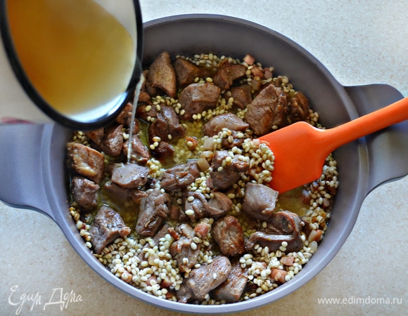 Затем в сотейник верните обжаренные кусочки мяса, всыпьте перловую крупу, влейте сидр и куриный бульон. Доведите до кипения и готовьте в течение 20 минут на слабом огне при закрытой крышке (периодически необходимо перемешивать). Если у вас нет сидра, то его можно заменить сухим белым вином, несладким яблочным соком, также вы можете 1 ст. л. яблочного уксуса развести в стакане воды.