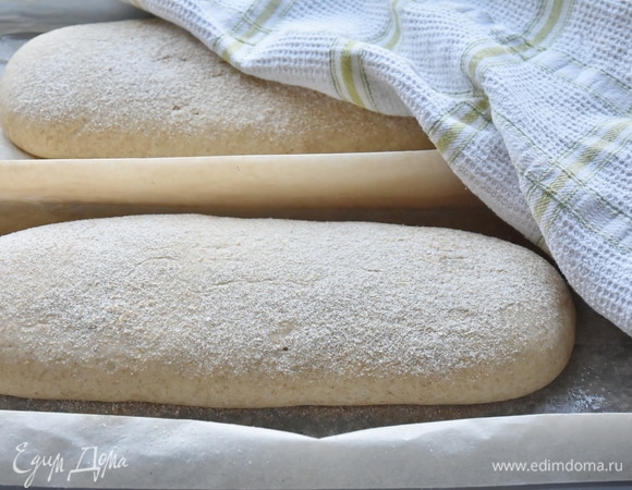 Готовое тесто разделить на две равные части и сформировать батоны. Уложить их на противень, выстеленный пергаментом, и сверху посыпать цельнозерновой или ржаной мукой. Накрыть хлеб кухонной салфеткой и оставить на 1–1,5 часа для подъема. Духовку разогреть до максимальной температуры (230–250°C). Уменьшить жар до 200–210°C. Выпекать чиабатту 25–30 минут. Остудить хлеб на решетке.