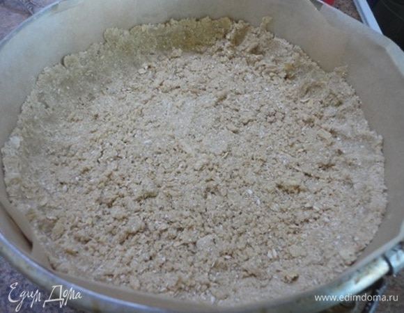 Большую часть крошки выложить в форму. Утрамбовать и сформировать бортики. В оставшуюся часть крошки добавить измельченные орехи, перемешать и пока убрать в холодильник.