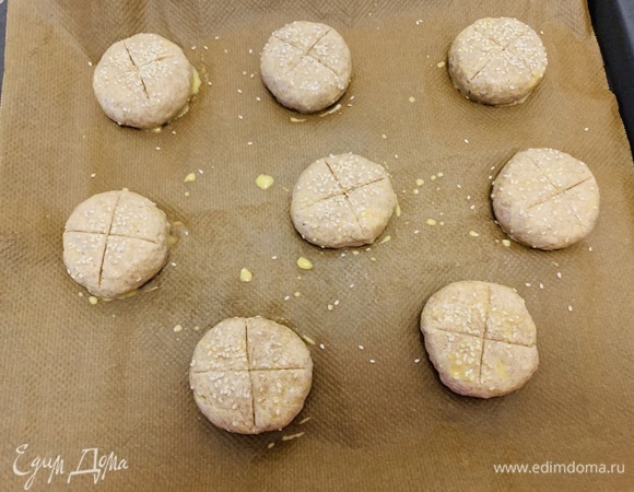 Тесто делим на 9 частей (около 70 г каждая). Скатываем шарики, ставим на противень, покрытый тефлоновой бумагой, слегка приплющиваем и смазываем желтком (или тем, чем вы любите смазывать тесто). Посыпаем любыми семенами. У меня кунжут. Сверху делаем крестообразные надрезы и ставим в духовку. Сразу заливаем в горячую форму на дне печи кипяток и быстро закрываем дверцу духовки. Через 8 минут убираем емкость с водой (аккуратно!). Сбавляем до 180°C и продолжаем выпекать еще минут 15–20 (ориентируйтесь по своей духовке, булочки должны быть слегка румяными).