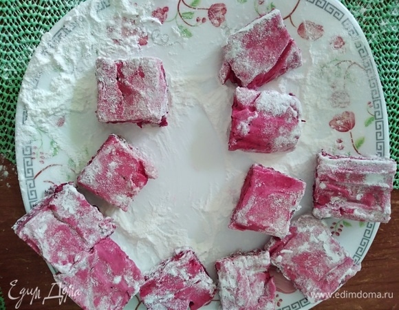 В тарелке перемешать пудру и крахмал. Нарезать маршмеллоу на квадратики и обвалять в этой смеси.