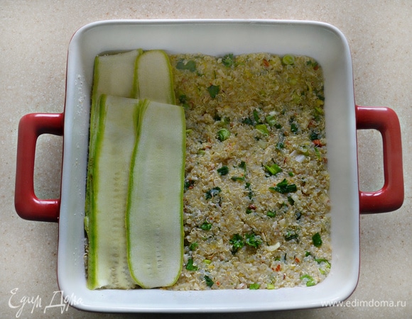 Форму для запекания (небольшую, но достаточно глубокую) смажьте оливковым маслом, можно также немного посыпать дно и бортики формы манной крупой. Выложите половину смеси с киноа в форму, разровняйте, слегка утрамбовывая. Сверху уложите пластины нарезанных кабачков, получится пару слоев внахлест. И далее — оставшуюся смесь из киноа, также разравнивая поверхность и утрамбовывая.