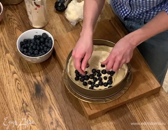 Разъемную форму застелить бумагой для выпечки, выложить тесто и прижать его руками, сверху равномерно распределить творожную начинку, затем голубику.  