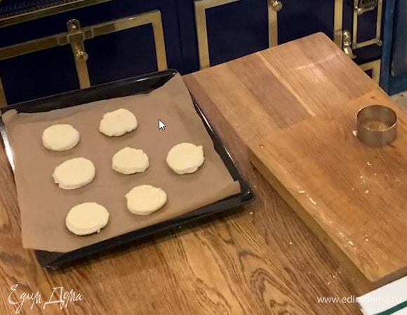 Сформировать из теста толстый пласт, кондитерским кольцом вырезать лепешки и выложить на противень, застеленный бумагой для выпечки.