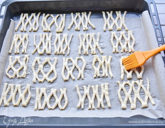 Каждый отдельный сегмент растянуть, чтобы раскрылся рисунок. Выложить заготовки на противень, застеленный пергаментной бумагой, и смазать их яичным желтком, смешанным с молоком. Выпекать печенье в разогретой до 200°C духовке 10 минут.