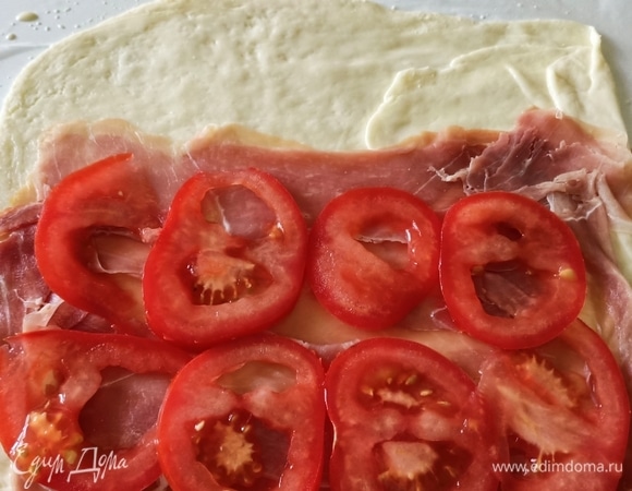 Аккуратно удалить верхний слой пергаментной бумаги, выложить слоями прошутто, томаты и снова прошутто.