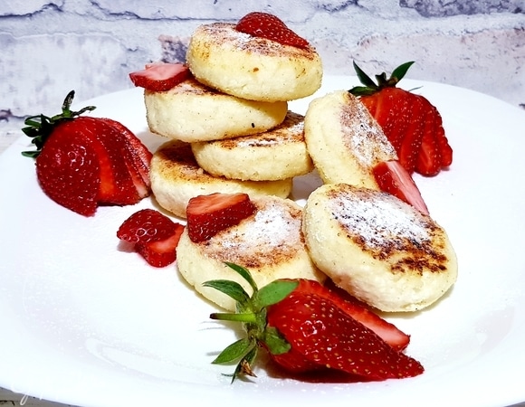 Посыпаем сырники сахарной пудрой. Подаем с клубникой и сметаной.