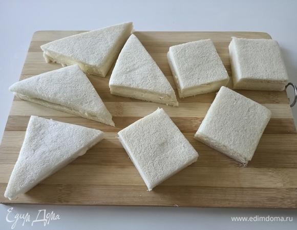 Слегка придавить руками. Обрезать корку и разрезать каждый бутерброд на квадраты или треугольники — что больше нравится.