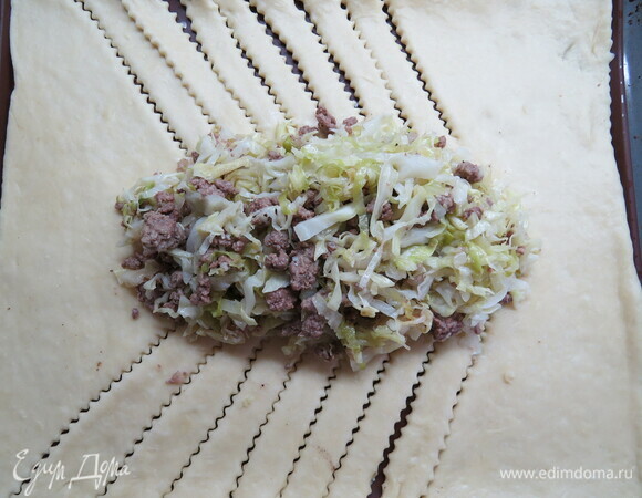 Переносим тесто на противень, застеленный пергаментом или силиконовым ковриком, иначе потом это сделать будет трудно. На середину выкладываем начинку. Начиная с углов, делаем надрезы до начинки толщиной около 2–3 см. Складываем их косичкой внахлест, оставляем только первые и последние.