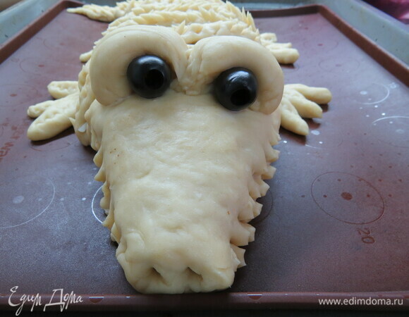 Формируем ноздри у крокодила, из обрезков теста лепим лапки и глаза-брови. Делаем клыки с помощью ножниц по краю челюсти.