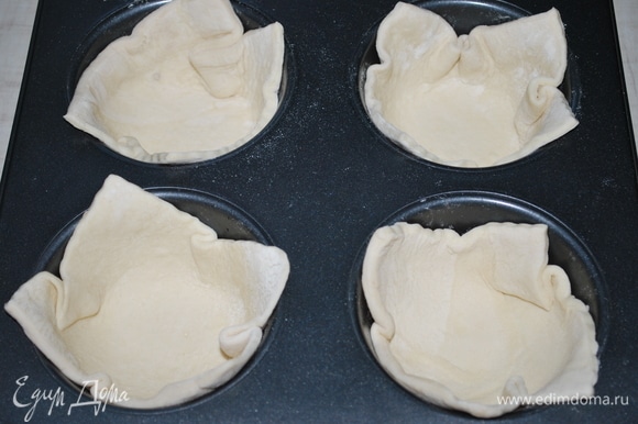 Пласт слоеного дрожжевого теста разрежьте на 4 квадрата. Форму для выпечки смажьте маслом и выложите тесто.