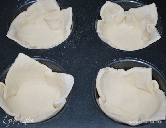 Пласт слоеного дрожжевого теста разрежьте на 4 квадрата. Форму для выпечки смажьте маслом и выложите тесто.