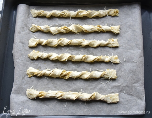 Выложить готовые спиральки из теста с начинкой на противень, застеленный пергаментной бумагой. Сверху смазать небольшим количеством оставшегося белка и посыпать тертым пармезаном. Выпекать в духовке, разогретой до 200–220°C, 10–12 минут.
