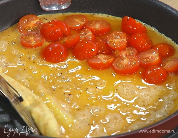 Влить яичную смесь в сковороду и прогревать на среднем огне. Когда омлет схватится по краям, на одну его половину выложить припущенные помидоры, накрыть второй половиной и жарить до готовности. 