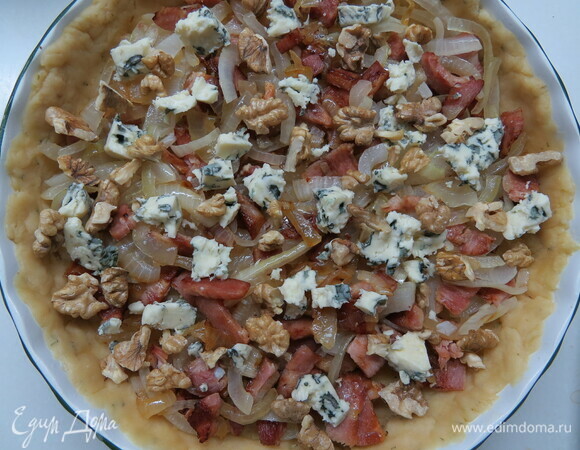 На раскатанное тесто выложить обжаренный лук, кубики ветчины, орехи и кусочки сыра с голубой плесенью (можно также использовать сыр бри).