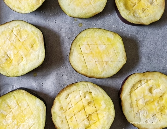 Один большой баклажан нарезать толщиной 1 см. Выложить на противень. Сделать надрезы, смазать оливковым маслом и посолить. Запекать 15 минут в разогретой до 180°С духовке.