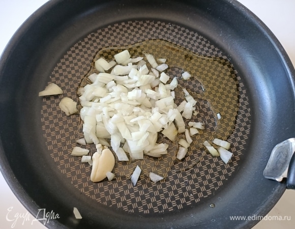 В разогретую сковороду налить оливковое масло. Чеснок очистить, раздавить тыльной стороной ножа и выложить в сковороду. Туда же отправляем нарезанный репчатый лук и слегка обжариваем.