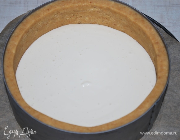 Достаньте из холодильника основу для чизкейка и выложите половину сырного слоя с ароматизированным молоком.
