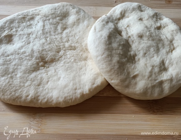 Через два часа, когда тесто увеличится в объеме, вымесить снова. Разделить на две равные части, выложить на пергаментную бумагу и раскатать.