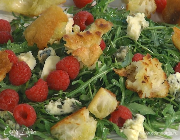 Выложить заправленную руколу на большую тарелку, сверху разложить кусочки сыра, добавить ягоды малины и крутоны.