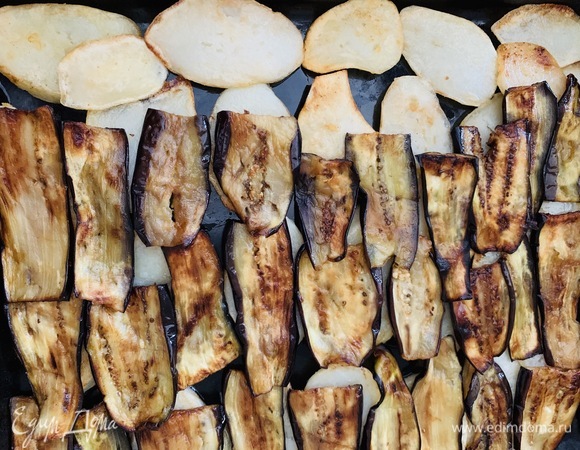 Собираем мусаку. На противень послойно выкладываем обжаренные дольки картофеля. На них кладем баклажаны.