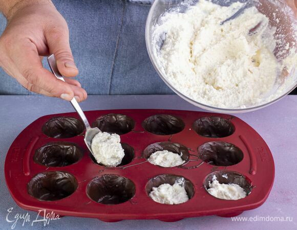 Достаньте формочки с шоколадной основой из морозилки. Каждую из них наполните творожной массой наполовину.
