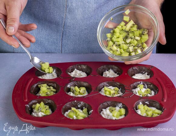 Добавьте кусочки нарезанного кубиками киви. Сверху выложите оставшийся творог. Разровняйте. 