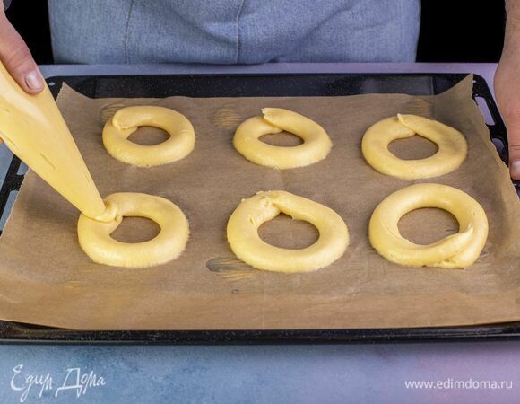 Выложите тесто в кондитерский мешок. Отсадите кольца на противень, застеленный пекарской бумагой.<br />
Выпекайте 15 минут при 220 °С, а затем еще 15 минут при 150 °С (убавляйте температуру, не открывая дверцу духовки). К этому моменту кольца должны приобрести золотистый оттенок.