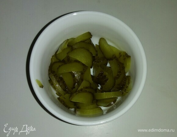 Соленый огурец разрезаем вдоль пополам, а затем нарезаем тонкими кусочками.