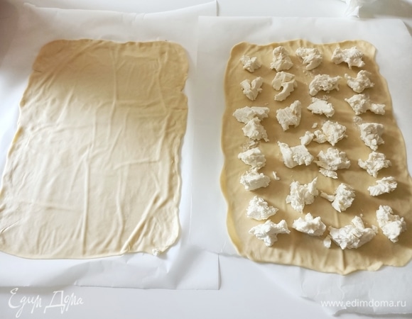 Достаем тесто, снова вымешиваем. Выкладываем на пергаментную бумагу и очень тонко раскатываем, должно получиться два прямоугольника одинакового размера. На один кладем сыр.