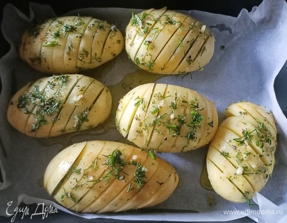 Форму для запекания застелить пергаментной бумагой, выложить на нее картофель. Полить заправкой, аккуратно раскрывая надрезы.
