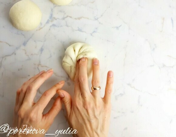 Смешиваем до растворения теплую воду (~37°C), дрожжи, соль, сахар и оливковое масло. Всыпаем просеянную муку. Хорошо вымешиваем тесто руками минут 7, до гладкости. Кладем его в чашку, накрываем пленкой и даем подняться в полтора раза (40–60 минут). Делим тесто на кусочки по 100 г. Формируем шарики. Для этого у каждого кусочка теста все края загибаем в центр.